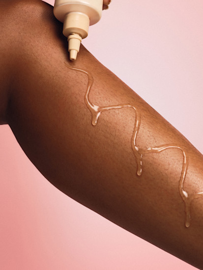 Foundation being applied in a zigzag pattern on skin against a pink background.