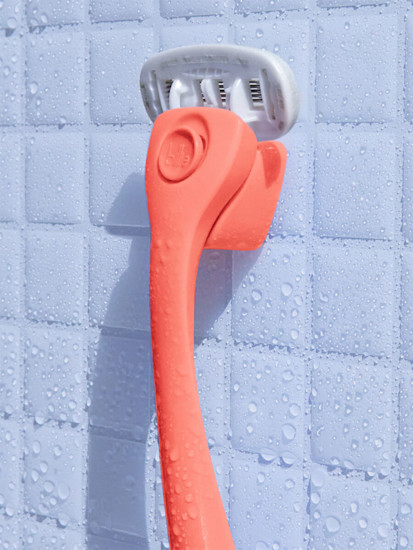 Coral razor hanging on a coral magnetic holder on a white shower tile
